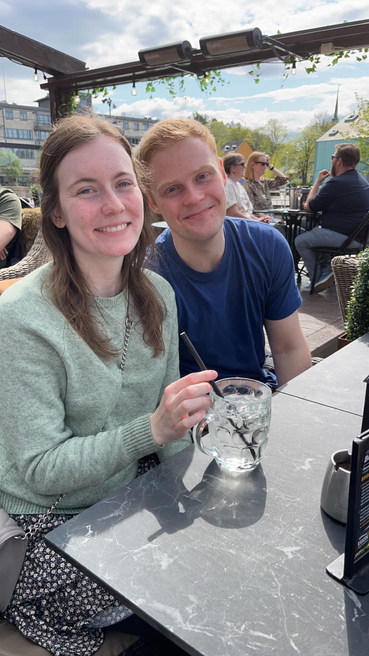 Kristine og Ola smiler sammen ved et kafébord utendørs