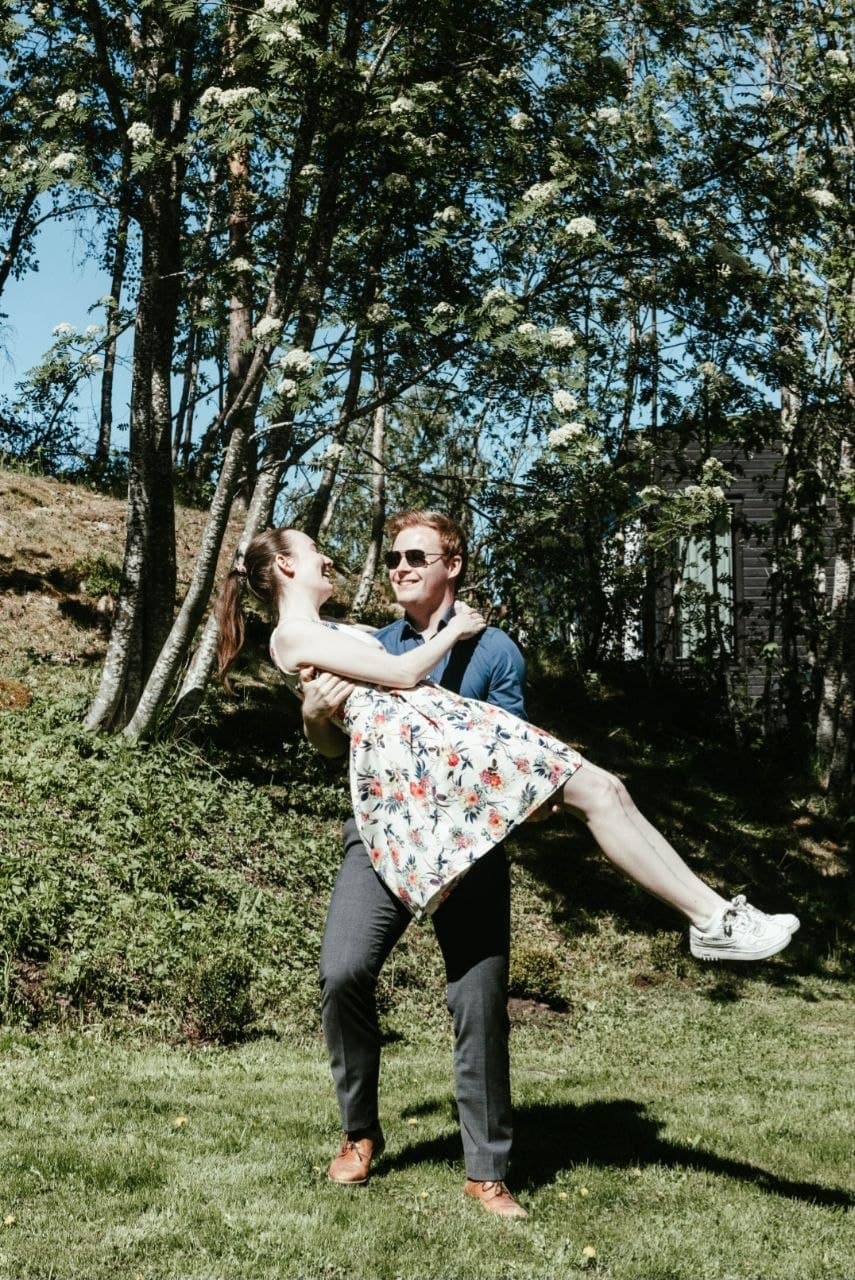 Ola løfter Kristine i blomstrete kjole på en solfylt gressplen