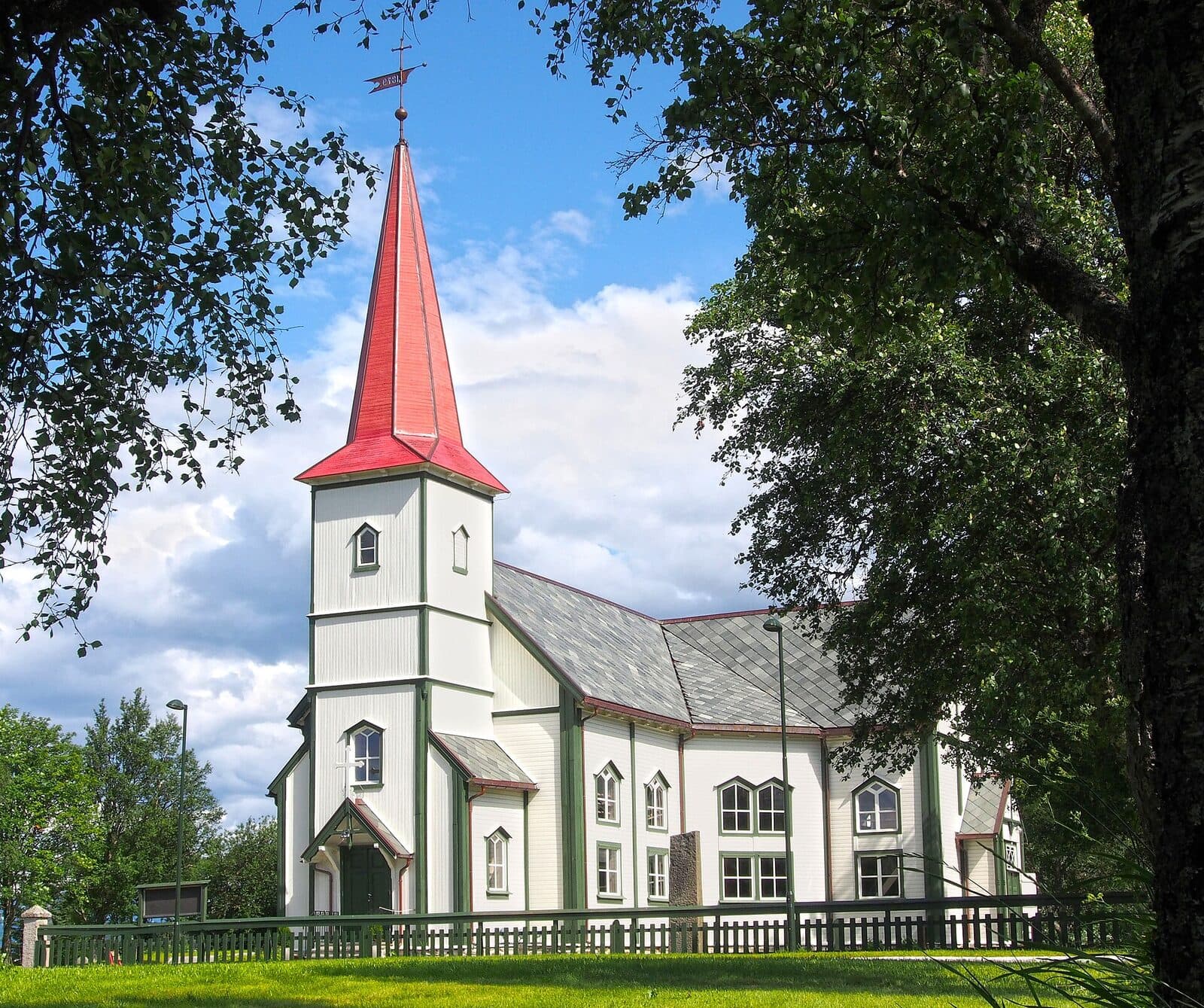 Nesna kirke med hvite vegger, rødt spir og grønne trær